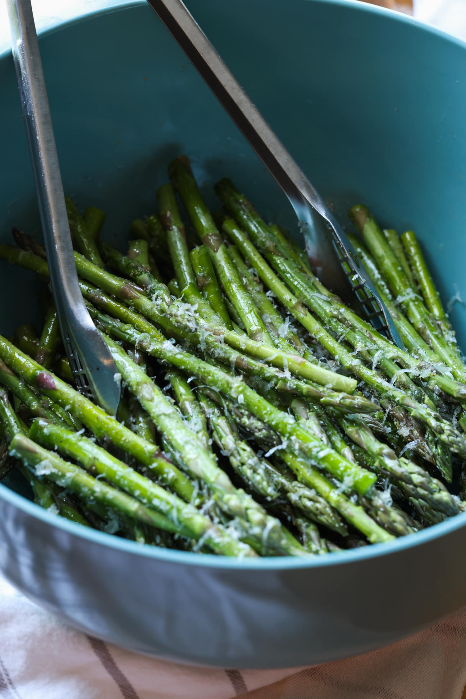 Make perfectly roasted Air Fryer Asparagus with Parmesan in 15 minutes! A healthy side dish that cooks up fast and easy in the air fryer. Asparagus spears are tossed with seasonings in a large blue bowl with metal tongs.
