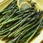Roasted air fryer asparagus on a yellow square serving platter, garnished with lemon slices.