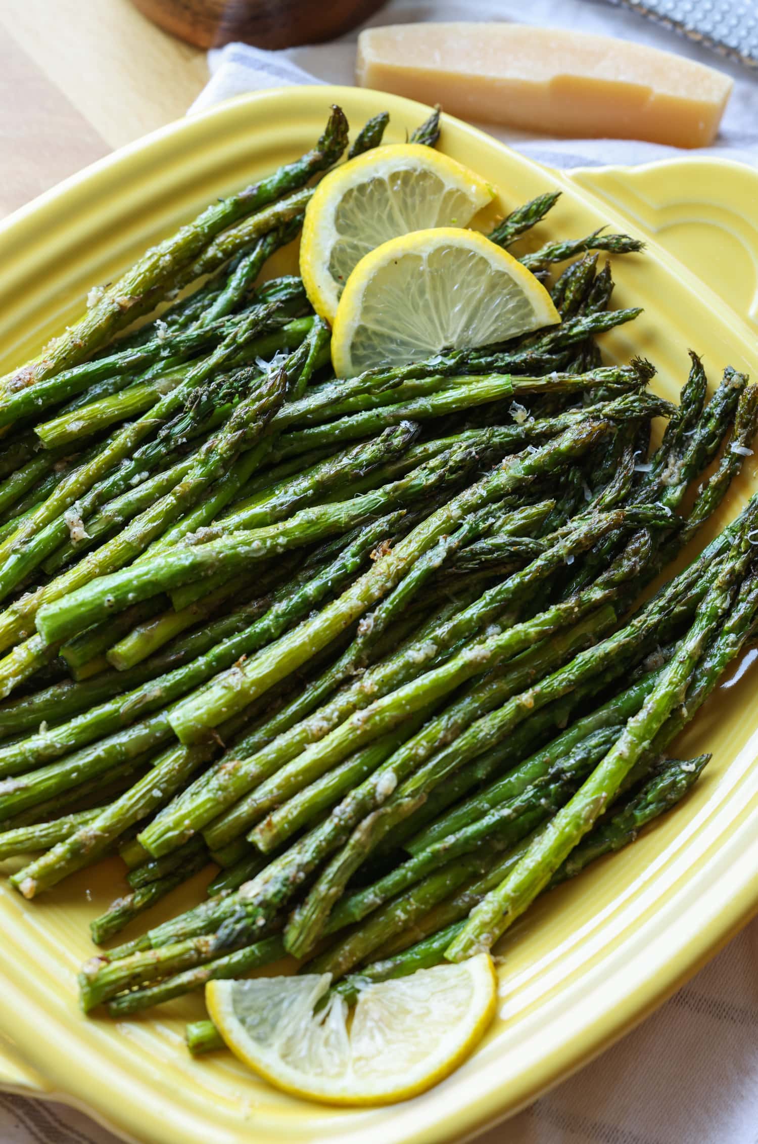 Make perfectly roasted Air Fryer Asparagus with Parmesan in 15 minutes! A healthy side dish that cooks up fast and easy in the air fryer. Roasted air fryer asparagus on a yellow square serving platter, garnished with lemon slices.