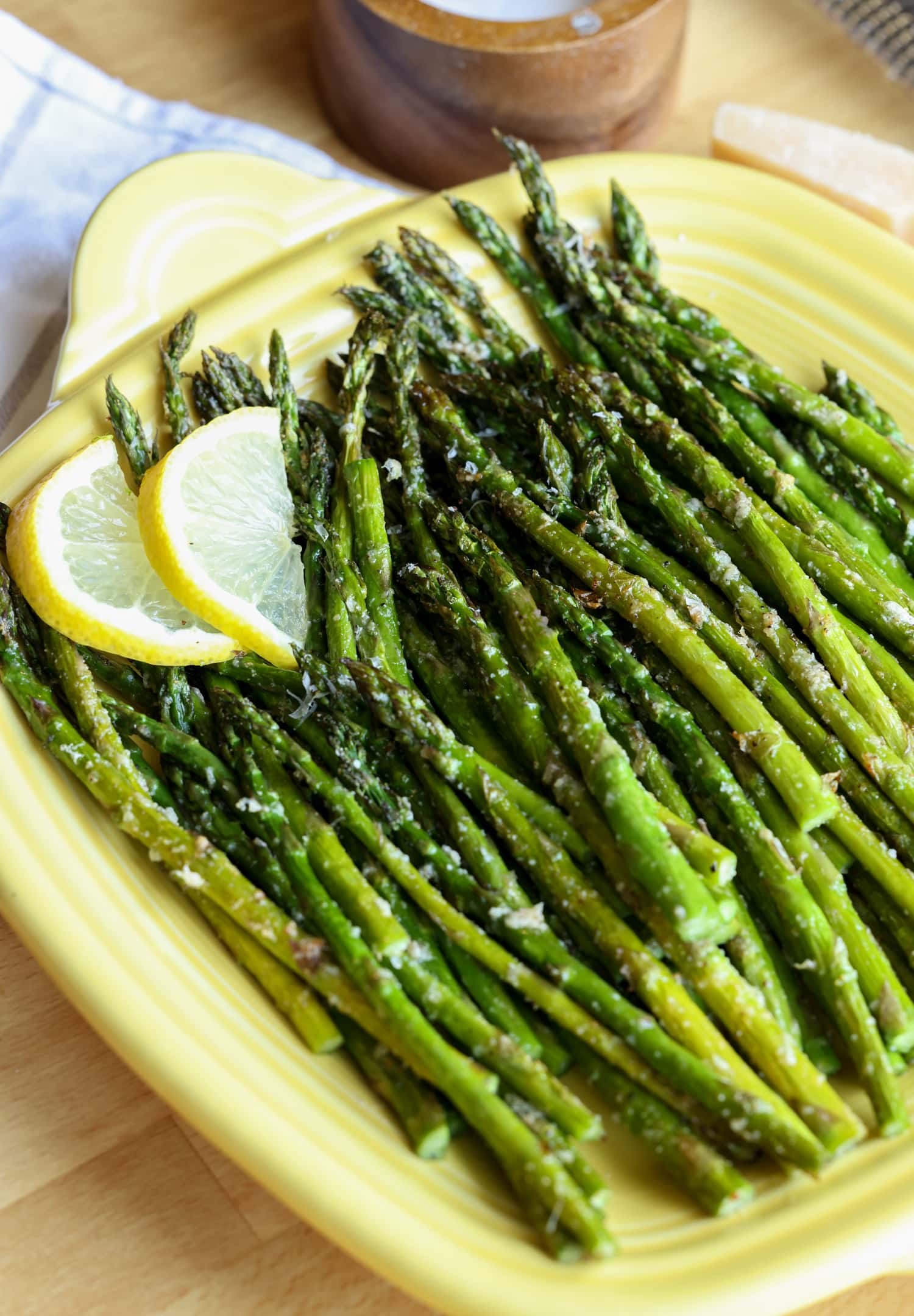 Make perfectly roasted Air Fryer Asparagus with Parmesan in 15 minutes! A healthy side dish that cooks up fast and easy in the air fryer. Roasted air fryer asparagus on a yellow square serving platter, garnished with lemon slices.