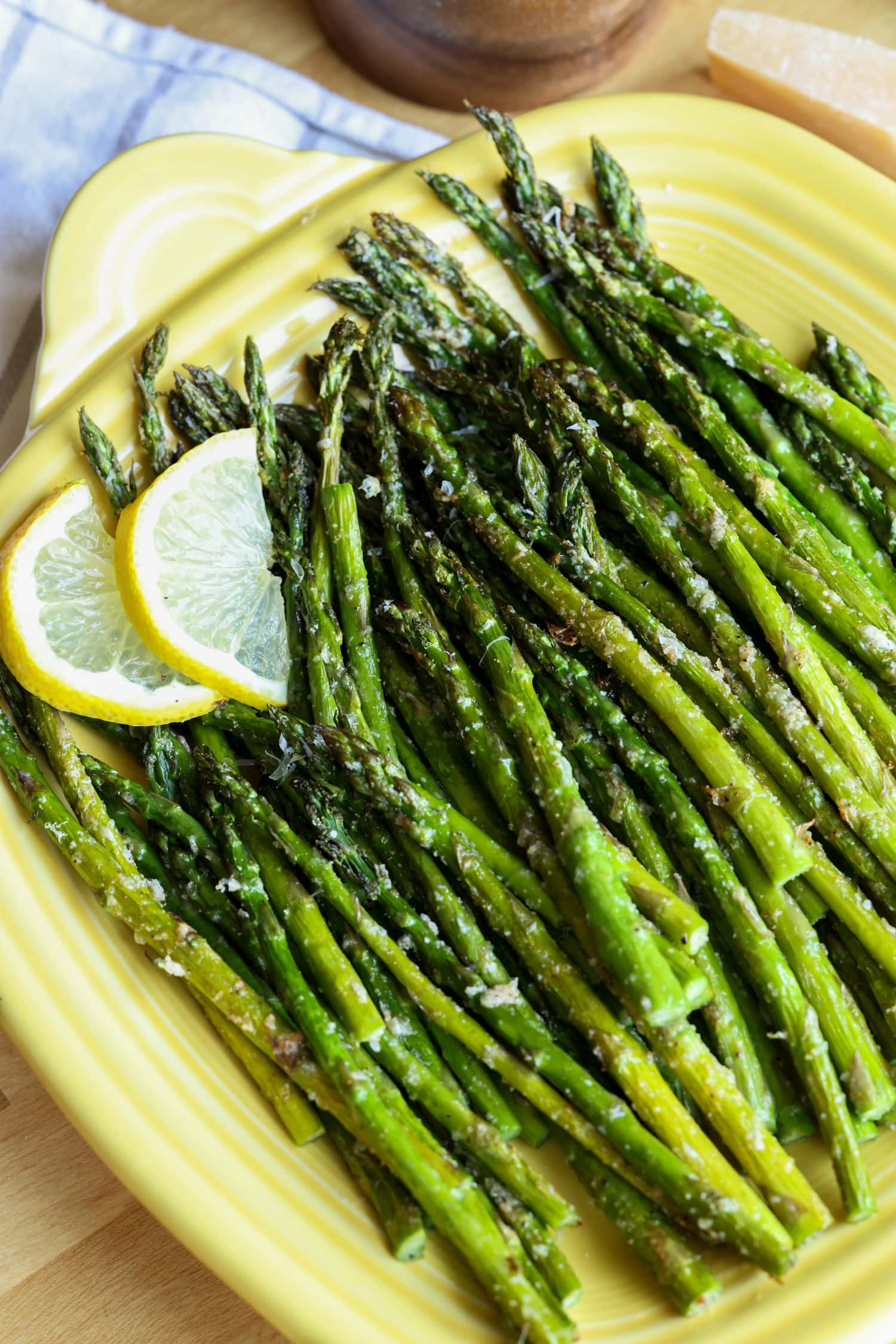 Make perfectly roasted Air Fryer Asparagus with Parmesan in 15 minutes! A healthy side dish that cooks up fast and easy in the air fryer. Roasted air fryer asparagus on a yellow square serving platter, garnished with lemon slices.