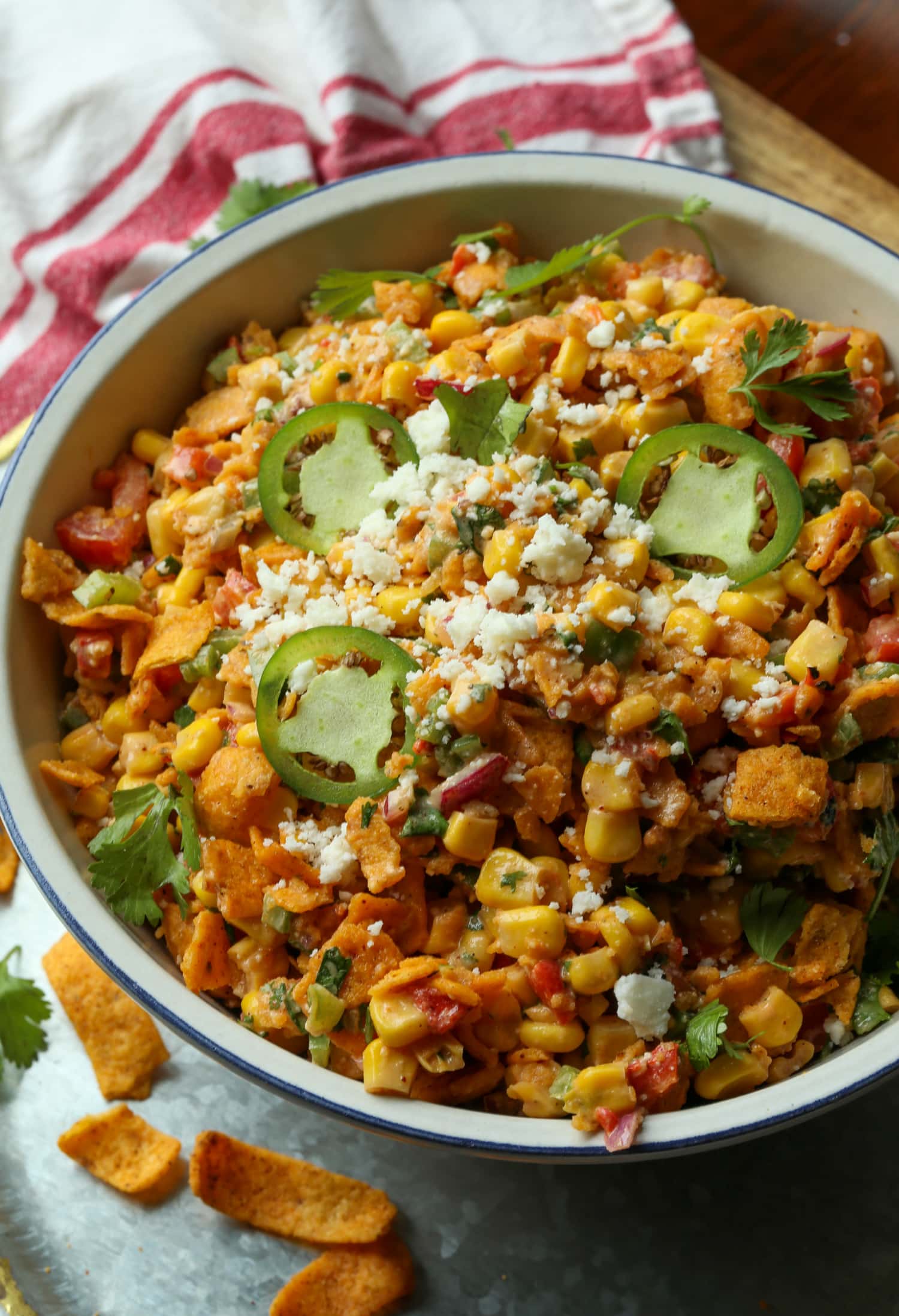 Spicy Frito Corn Salad is a fresh and zesty summer salad recipe loaded with sweet corn, crisp veggies, chili heat, and crunchy Fritos! Spicy Frito corn salad topped with cotija cheese and sliced jalapeños in a large white salad bowl.