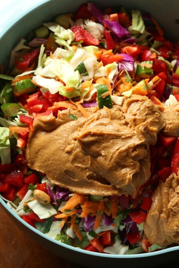 Peanut butter dressing is added to a bowl of rainbow crunch salad.
