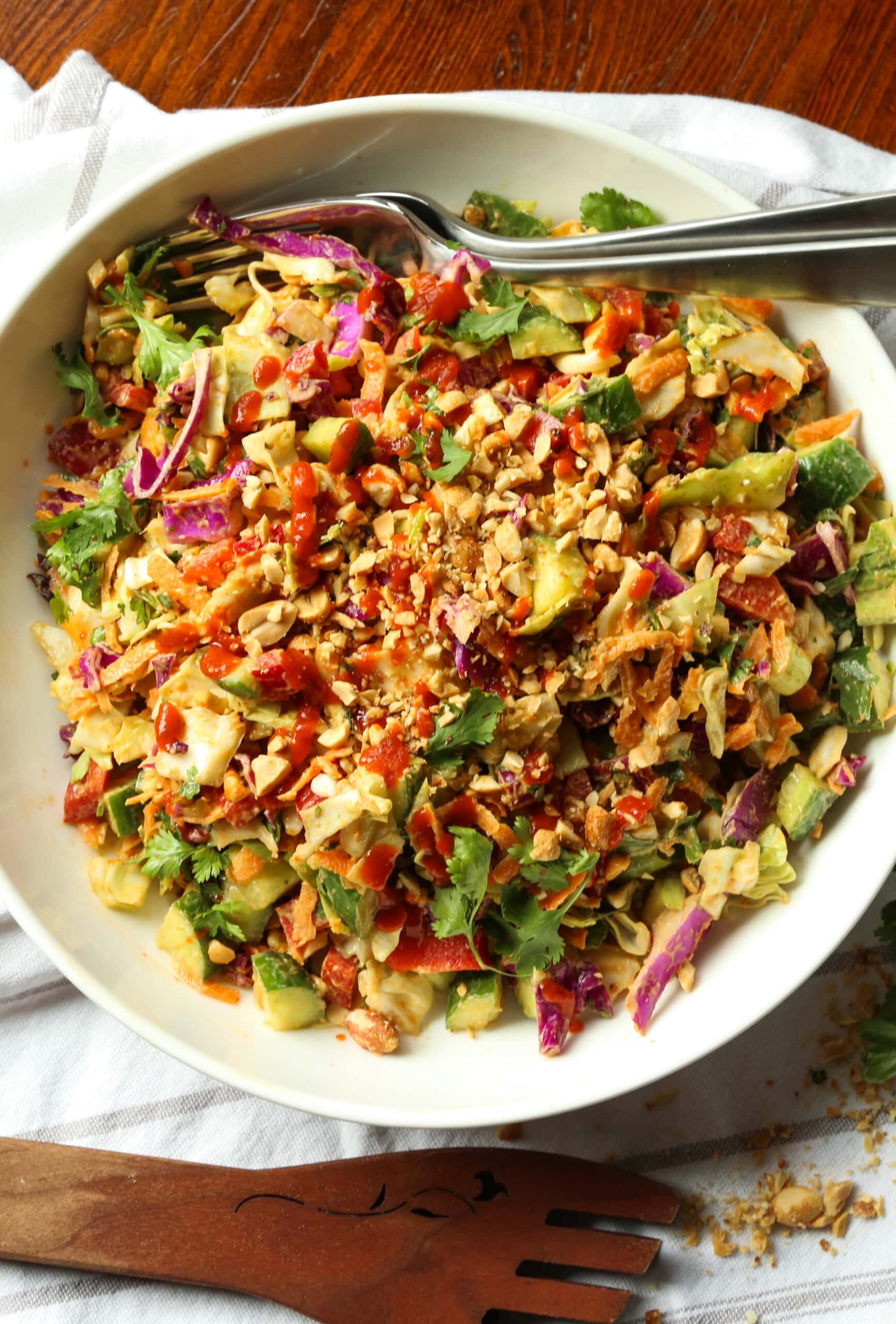Eat the rainbow with this Rainbow Crunch Cabbage Salad tossed in deliciously spicy Thai-style peanut dressing! A fresh and easy side dish. Rainbow crunch salad in a large white bowl, with a fork.