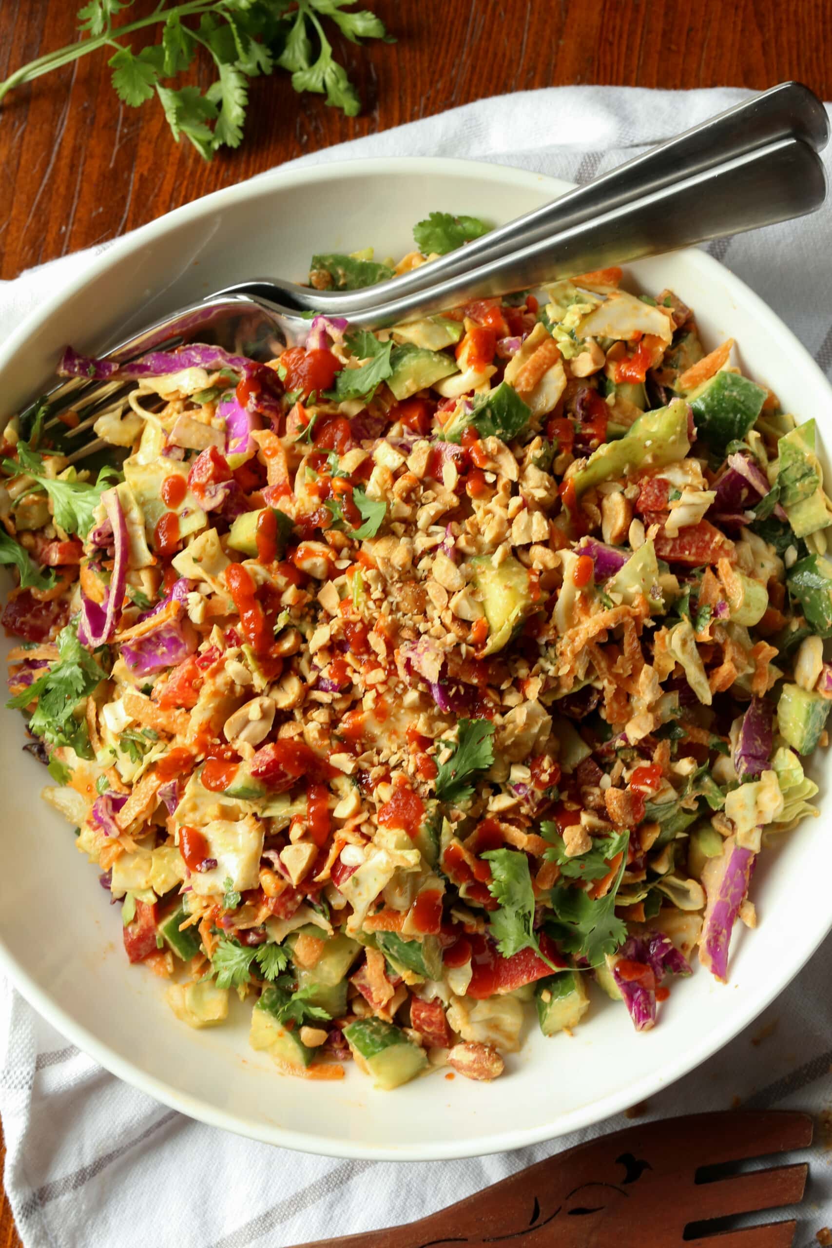 Eat the rainbow with this Rainbow Crunch Cabbage Salad tossed in deliciously spicy Thai-style peanut dressing! A fresh and easy side dish. Rainbow crunch salad in a large white bowl, with a fork.