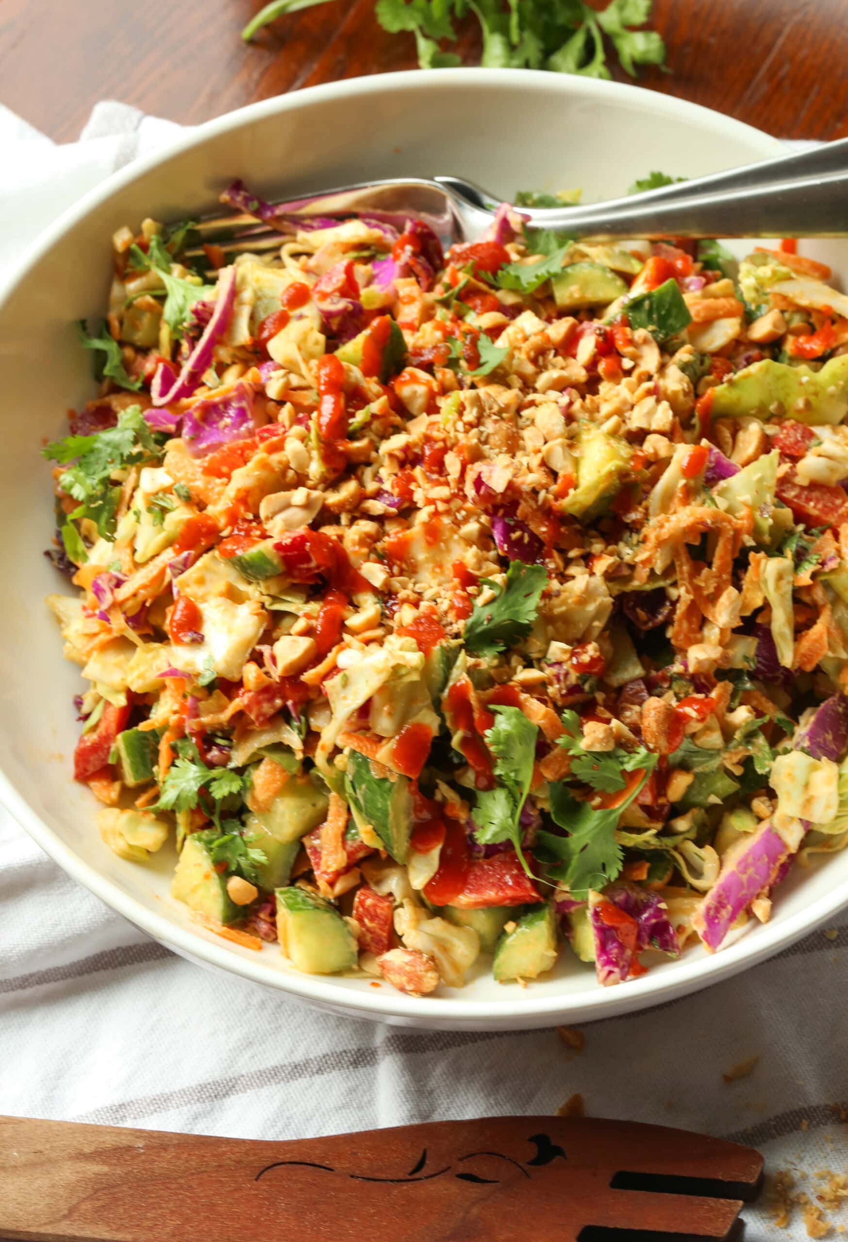 Eat the rainbow with this Rainbow Crunch Cabbage Salad tossed in deliciously spicy Thai-style peanut dressing! A fresh and easy side dish. Rainbow crunch salad in a large white bowl, with a fork.